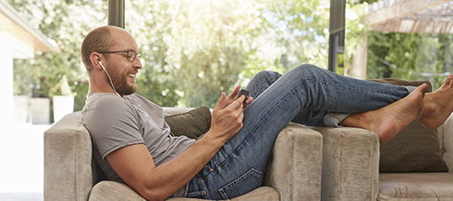 Side view image of a happy mature man using digital tablet while sitting on the sofa at home. Caucasian man relaxing on couch looking at tablet pc and smiling.